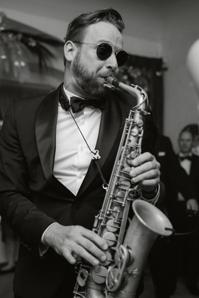 Schwarz-weiß: Saxophonist mit Sonnenbrille spielt bei der Hochzeitsfeier.